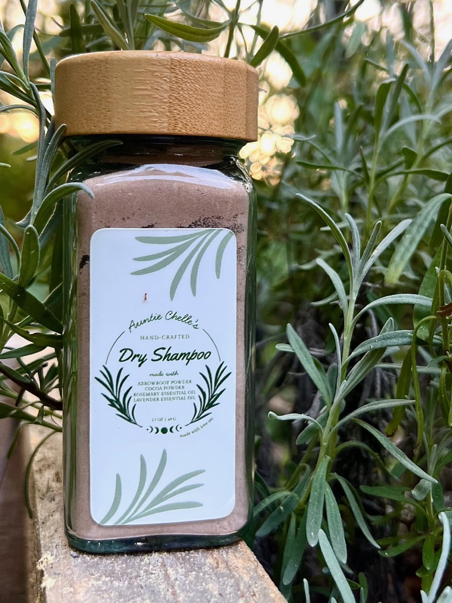 A glass jar of Auntie Chelle's Dry Shampoo with a bamboo lid, standing in a lavender bush at sunset
