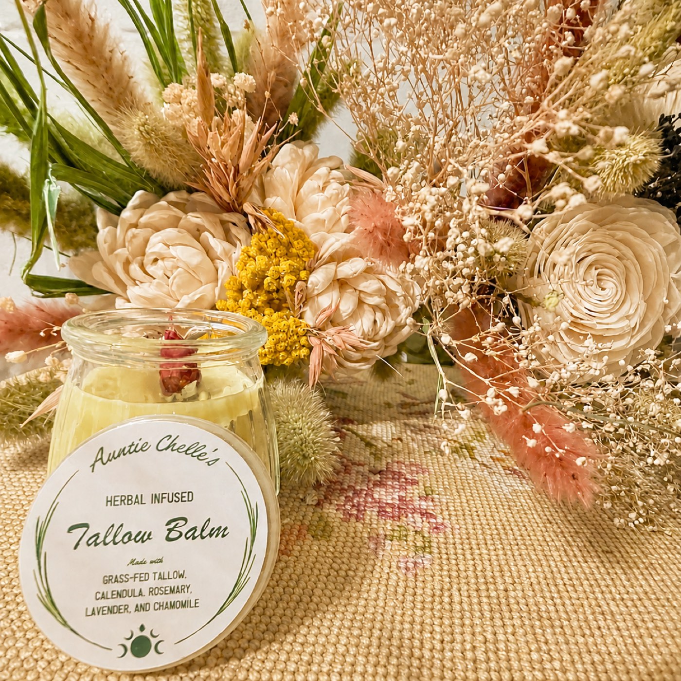 A jar of Tallow Balm beside a bunch of dried flowers
